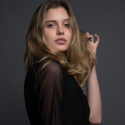 rafaella-mendes-diniz-et_78QkMMQs-unsplash A young woman with long, blonde hair, wearing a black top, looking directly at the camera with a confident expression.